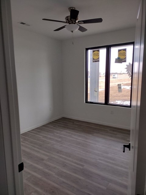 A room with a ceiling fan and a window overlooking a construction site.