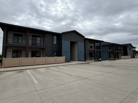 A parking lot in front of a building with grey and blue exterior.