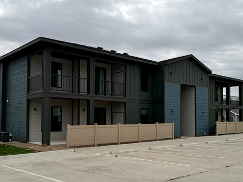A parking lot in front of a grey and blue building.