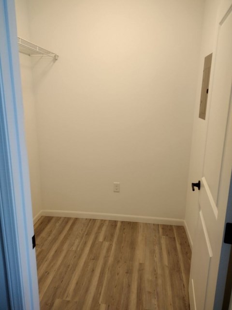 A white hallway with a wooden floor and a door on the right.