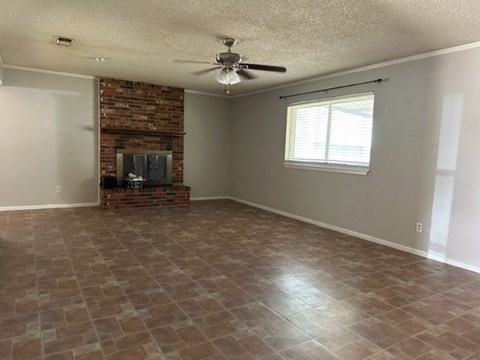 an empty living room with a brick fireplace and a ceiling fan