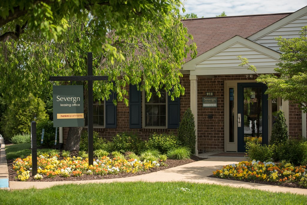 Exterior view of a brick leasing office with windows, beautiful trees and colorful flowers at Severgn Apartments in Exton, PA.