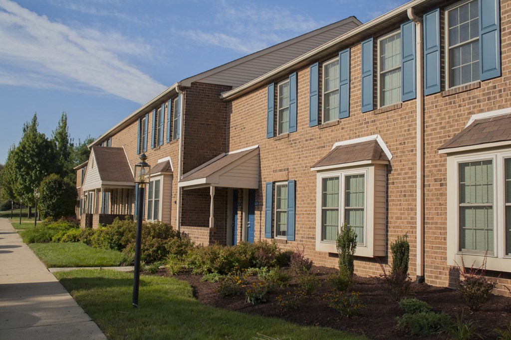 An exterior view of our Severgn's two-story brick apartment buildings with beautiful landscaping lining a sidewalk.