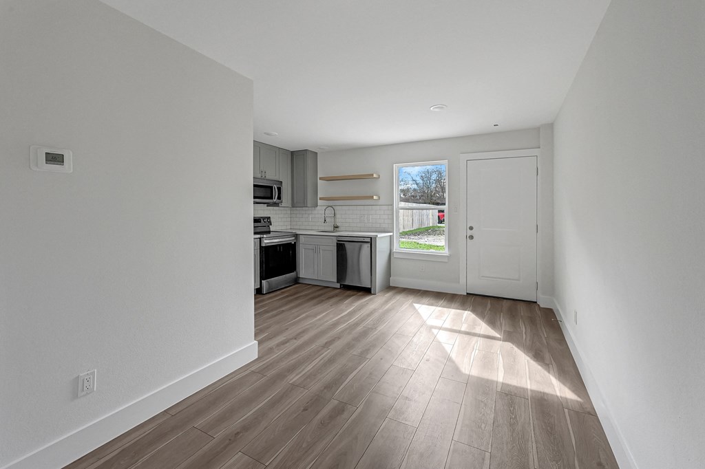 a living room and kitchen with white walls and wood floors