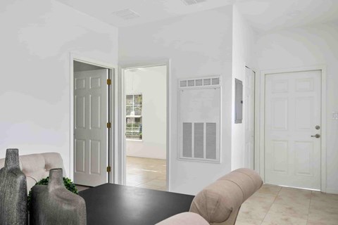 A room with a white door, a window with blinds, and a table with two vases on it.