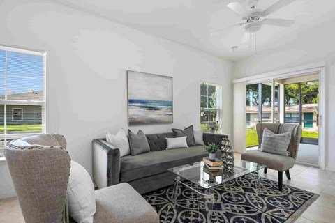 A living room with a grey couch, a glass coffee table, and a ceiling fan.