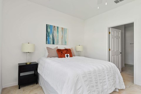 A bedroom with a white bed and a painting on the wall.