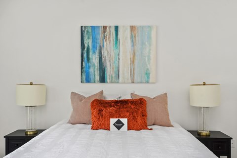 A bed with a white comforter and a painting above it.