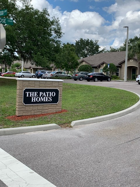 A sign for The Patio Homes is in front of a grassy area.