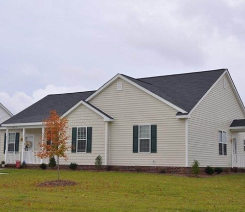 A house with a grey roof and white siding with green shutters.