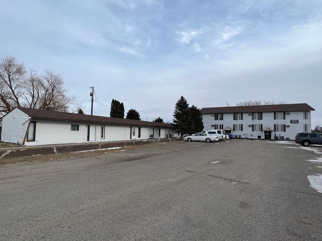 A parking lot in front of a white building with a few cars parked.