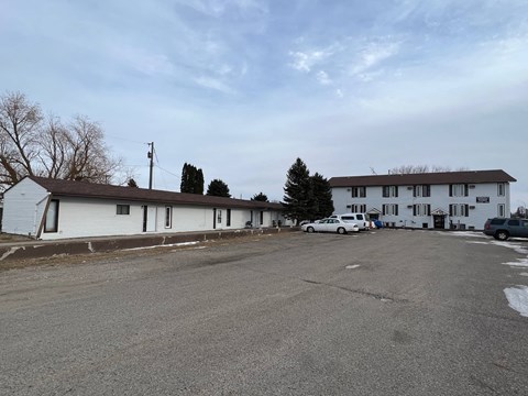 A parking lot in front of a white building with a few cars parked.