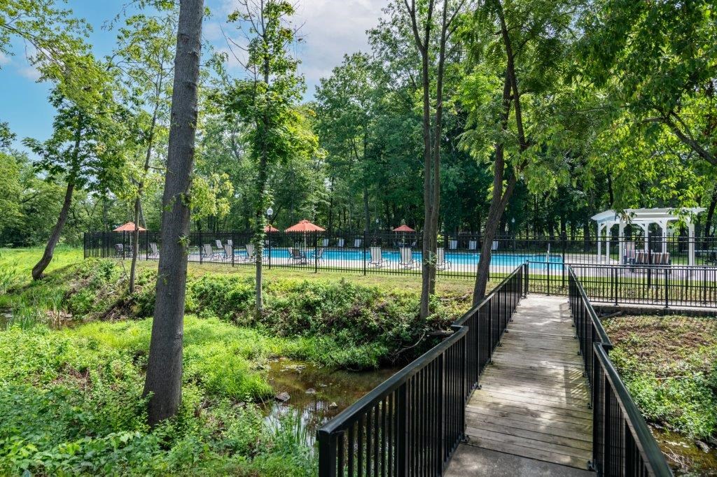 a wooden bridge over a river in a park with a swimming pool