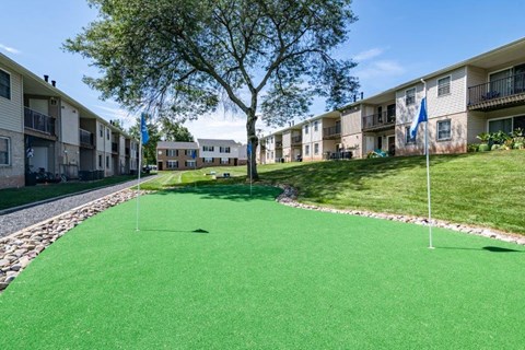 a putting green with two golf clubs in front of an apartment building