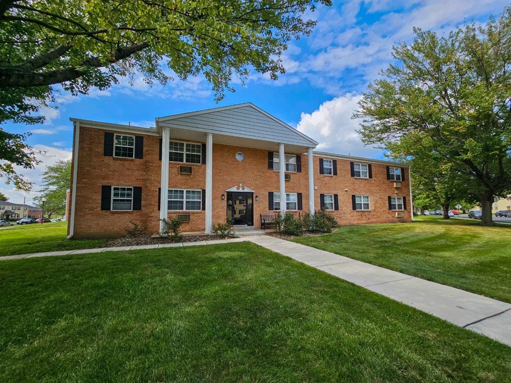 the front of a brick building with a sidewalk and grass