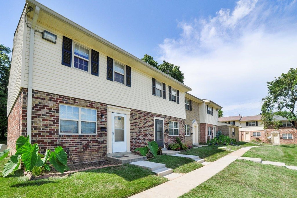a brick and white apartment building with grass and a sidewalk