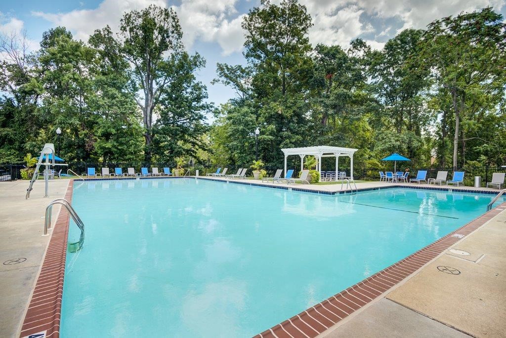 a large swimming pool with chairs and trees in the background