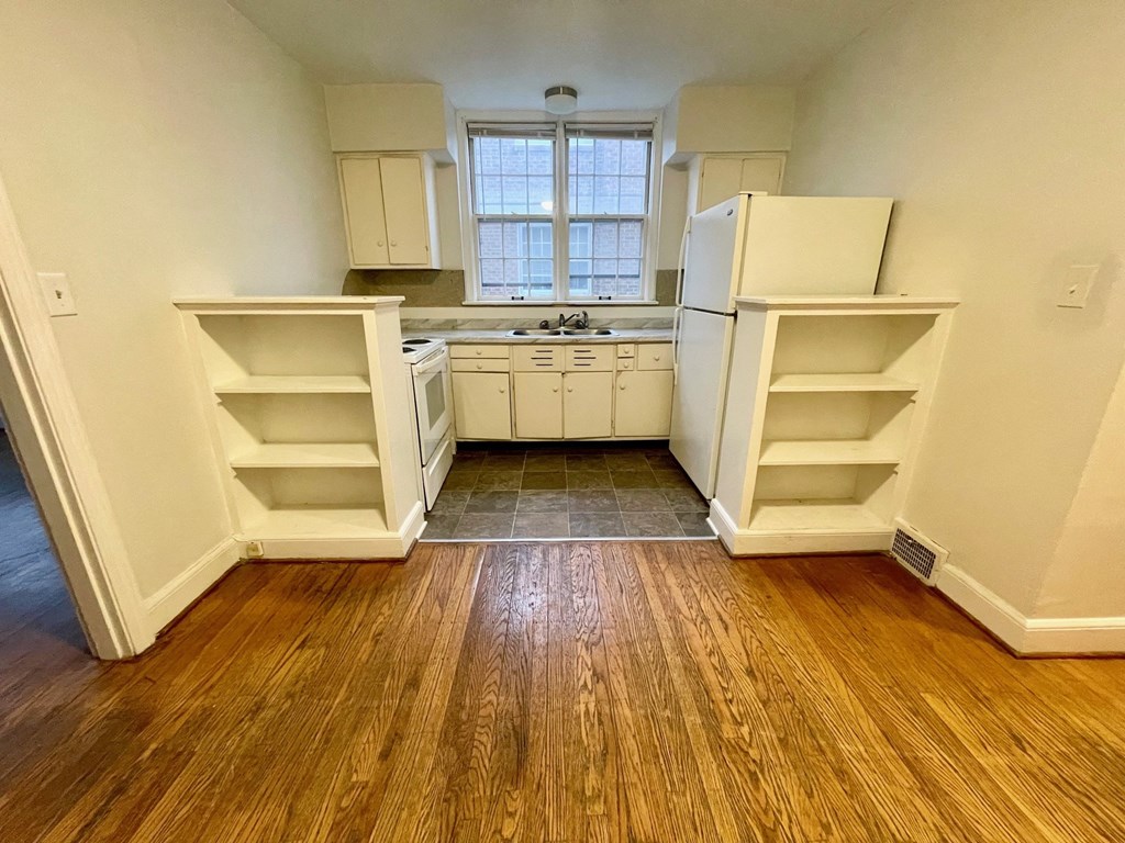 A kitchen with white appliances and wooden floors.
