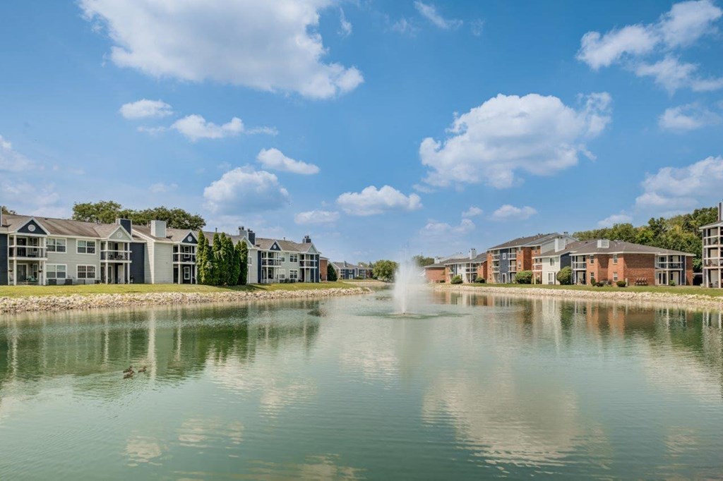 a fountain is in the middle of a lake with apartment buildings