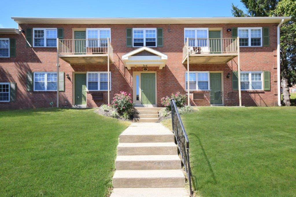 the front of a red brick house with a green lawn and stairs