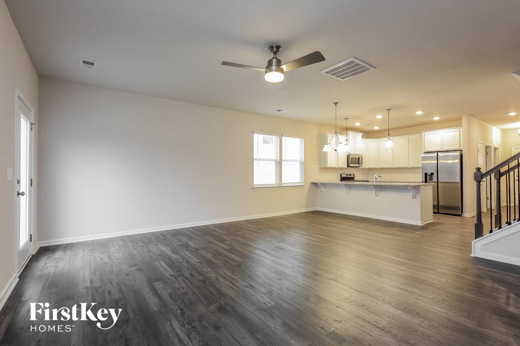 an empty living room and kitchen with wood flooring and a ceiling fan