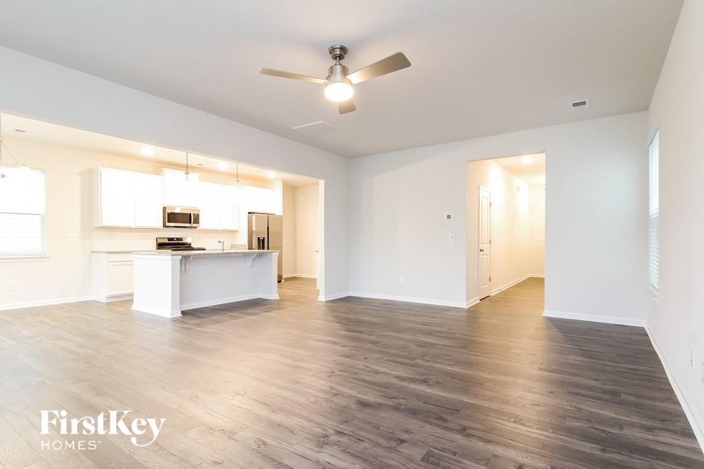 an empty living room with a ceiling fan and a kitchen