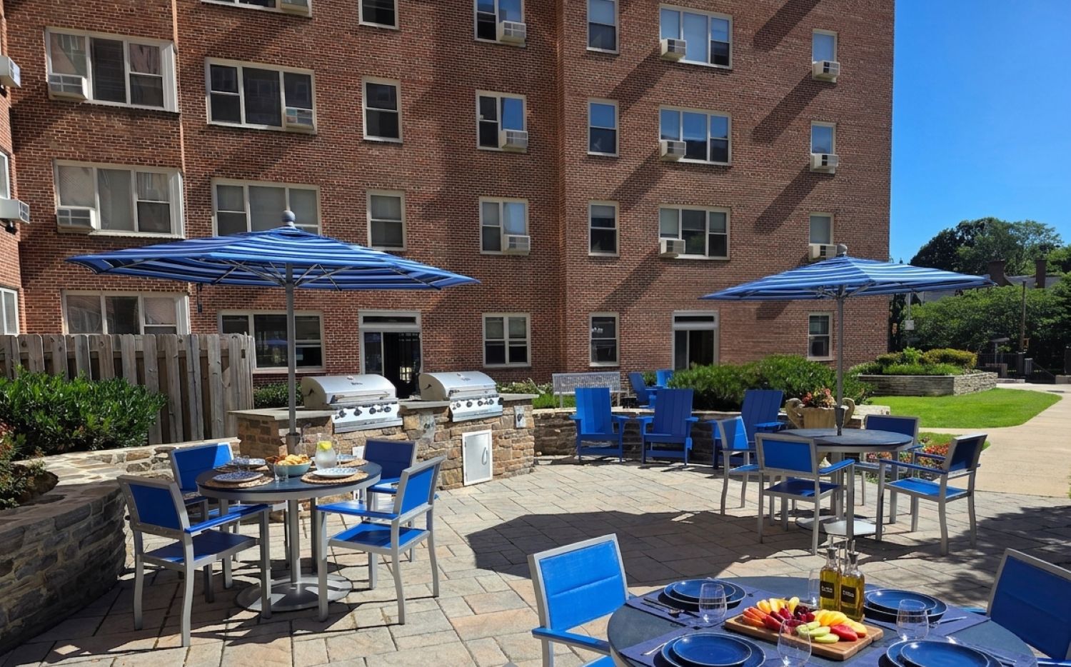 A patio with blue chairs and umbrellas is set up outside a brick building.