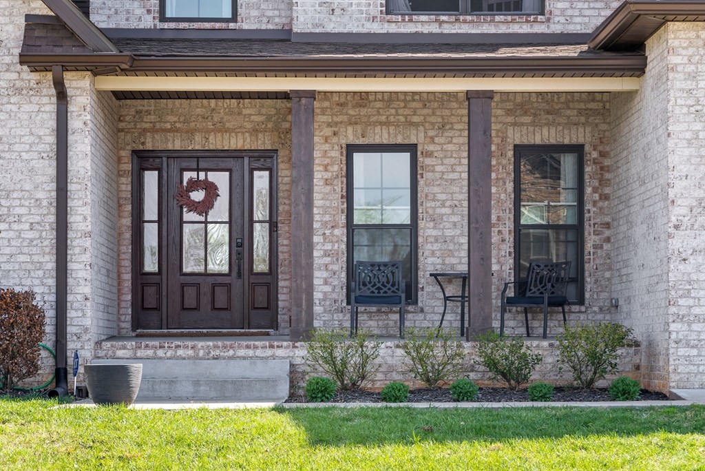 a front porch of a brick house with brown doors and windows