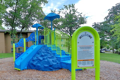 a playground with a blue and yellow slide and a sign