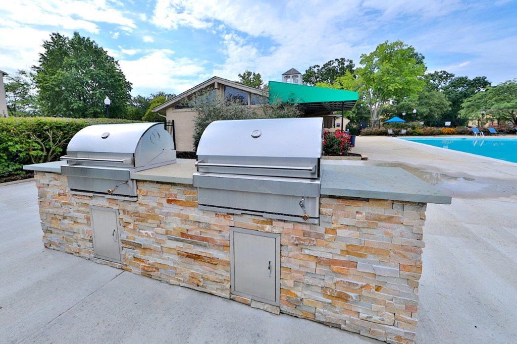 a stone bar with two grills next to a swimming pool