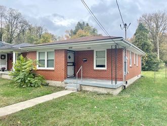 a small brick house with a porch and a lawn