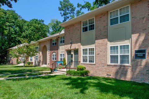 the front of a brick apartment building with grass and trees