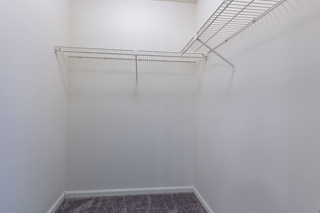 a walk in closet with white walls and a wire rack