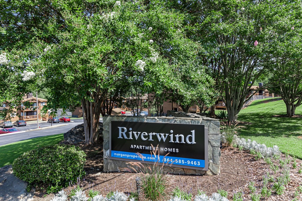 a sign for riverwind apartments in a park with trees