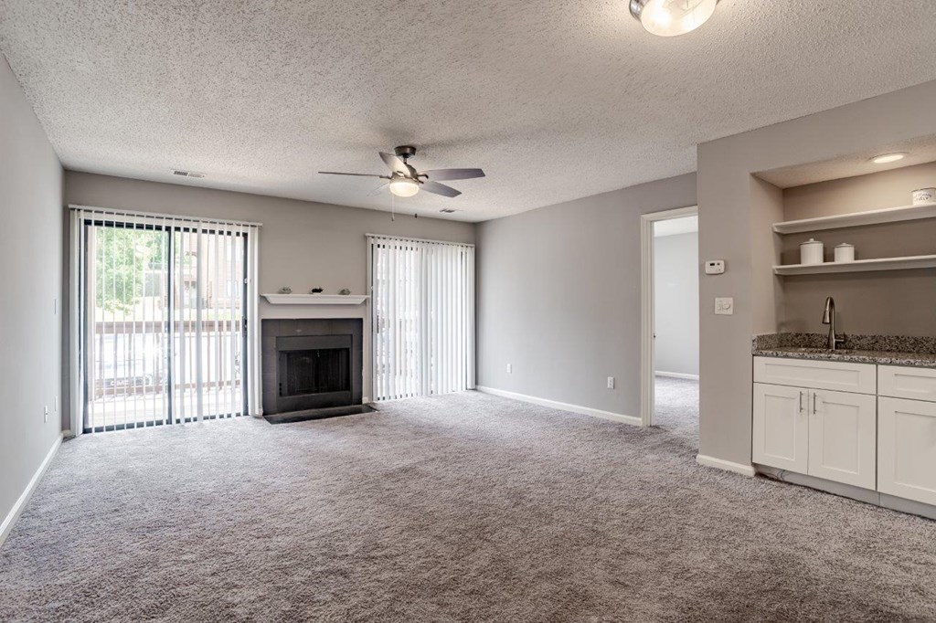 A spacious living room with a fireplace and a kitchen area in the background.