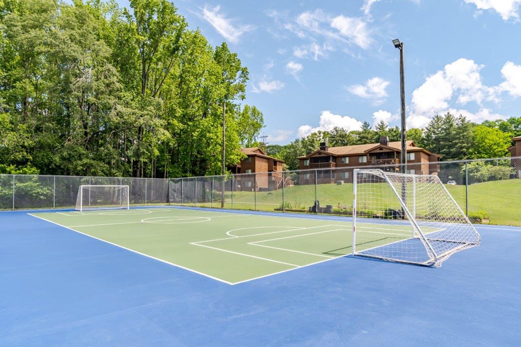 A blue tennis court surrounded by a fence and trees.