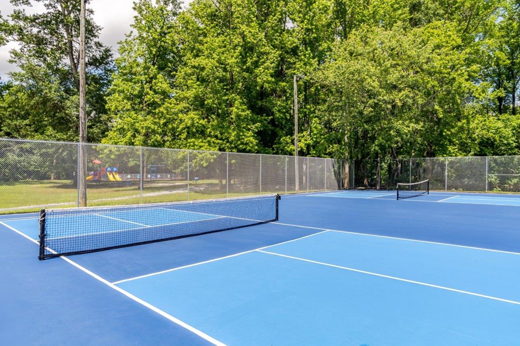 A blue tennis court surrounded by a fence and trees.