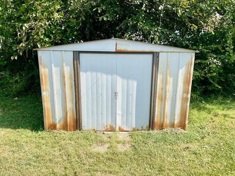 A rusted metal shed sits in a grassy field.