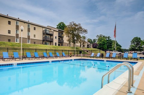 A swimming pool with blue water and a row of blue lounge chairs.