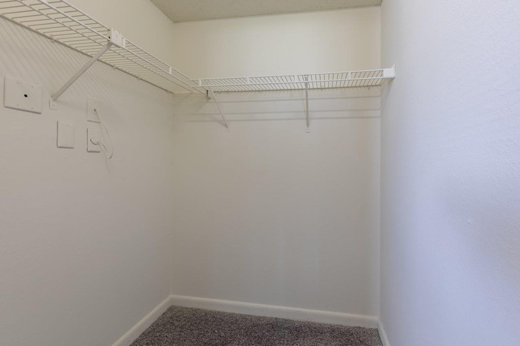 a walk in closet in a white room with a rack on the wall