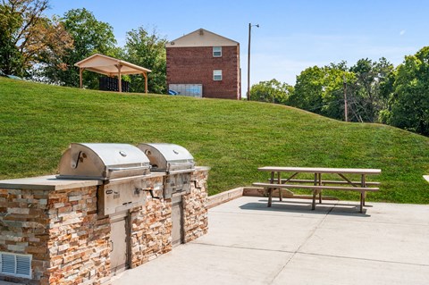 a picnic table and barbecue grill on a patio with a building in the background