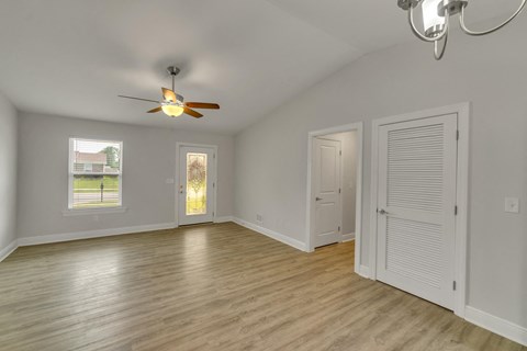 an empty living room with a ceiling fan and a door to a closet