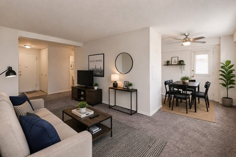 A living room with a grey carpet and a white ceiling fan.