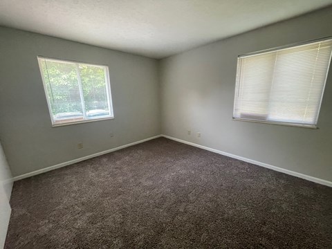 an empty room with carpet and two windows