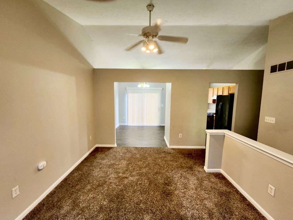 an empty living room with carpet and a ceiling fan