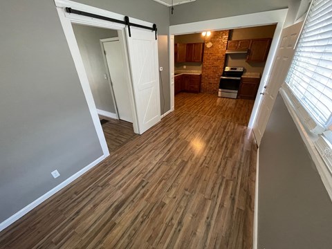 an empty living room with wood flooring and a door to a kitchen