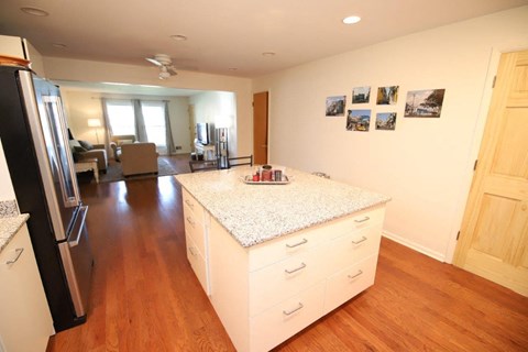 A kitchen with a refrigerator on the left and a counter with a white granite top.