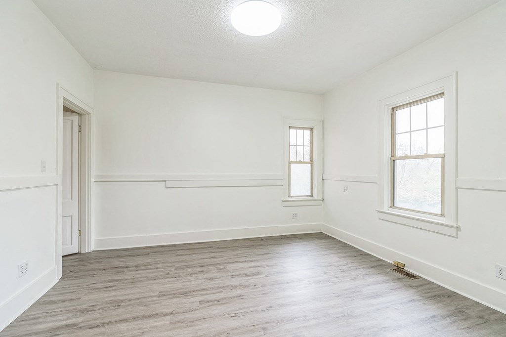 A large empty room with wooden floors and two windows.