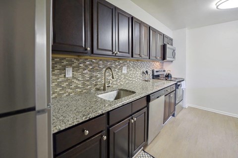 A kitchen with dark brown cabinets and a granite countertop.