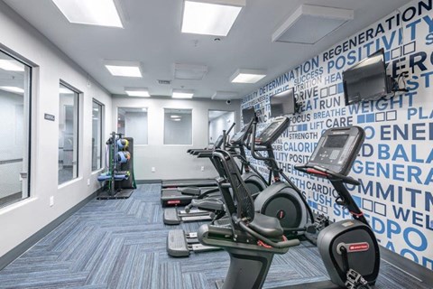 a gym with cardio machines and a wall covered in words
